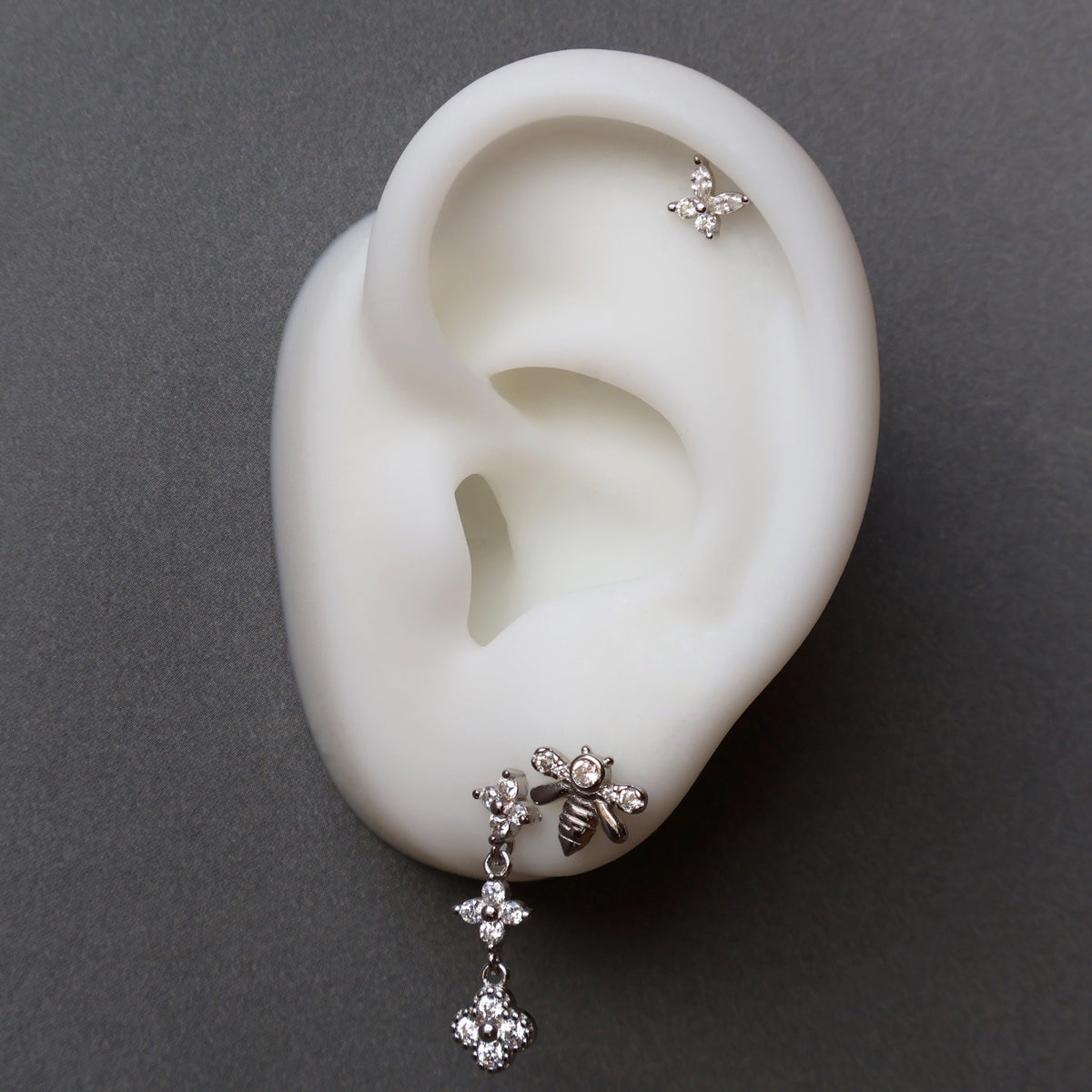Nature-inspired silver ear piercing stack on a model, showcasing a crystal dangle stud, a sparkling bee piercing, and a delicate floral helix stud.