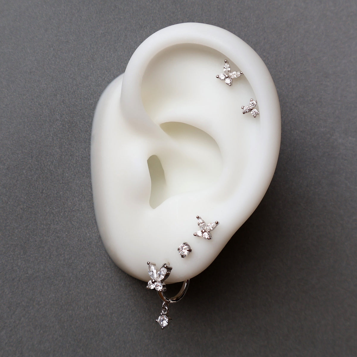 An elaborate silver ear piercing stack by JULE on a model, showcasing a crystal butterfly dangle hoop, tiny round and butterfly lobe studs, and a stunning double butterfly helix piercing.
