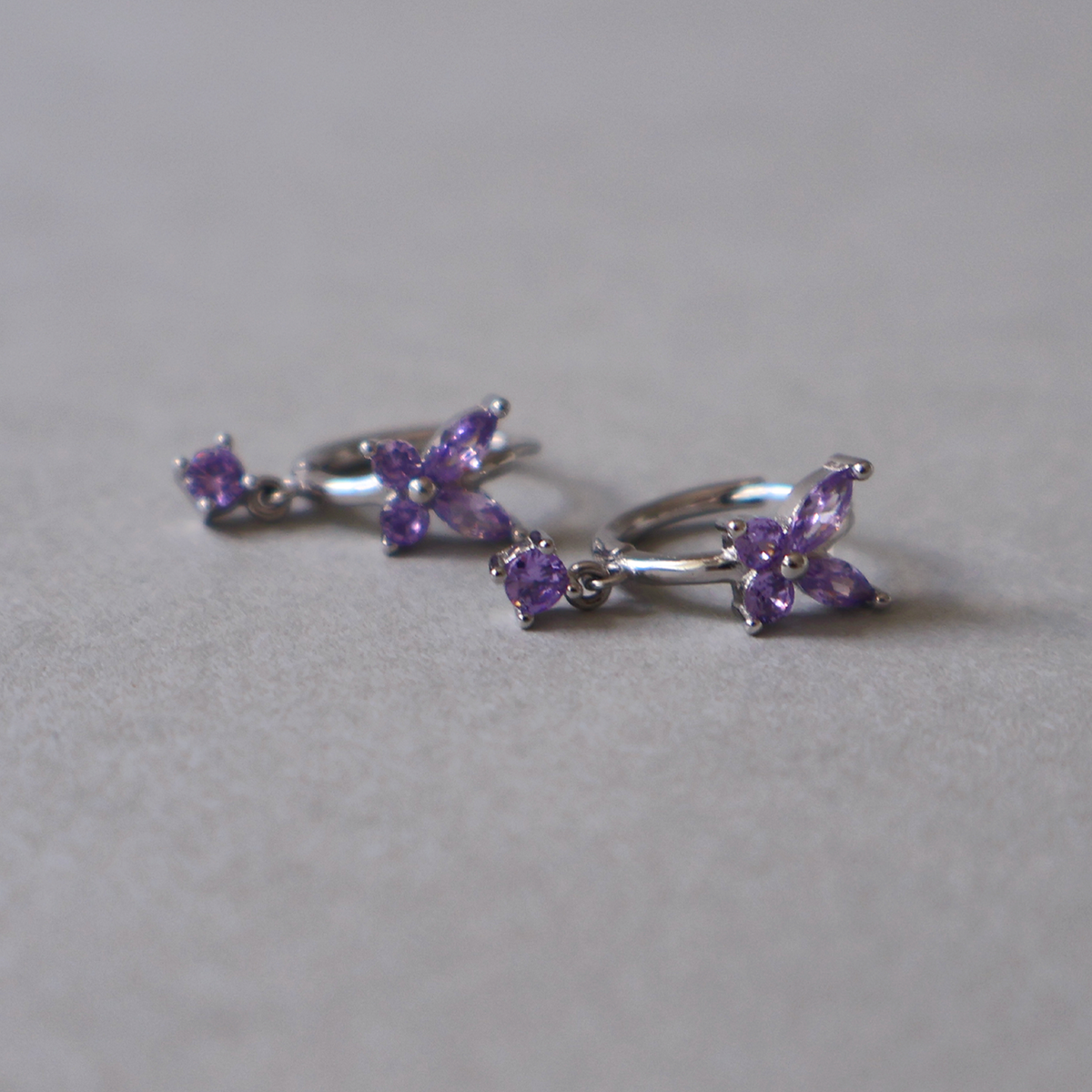 925 sterling silver hoop earrings featuring a purple cubic zirconia butterfly design and a small dangling purple stone, resting on a light neutral background