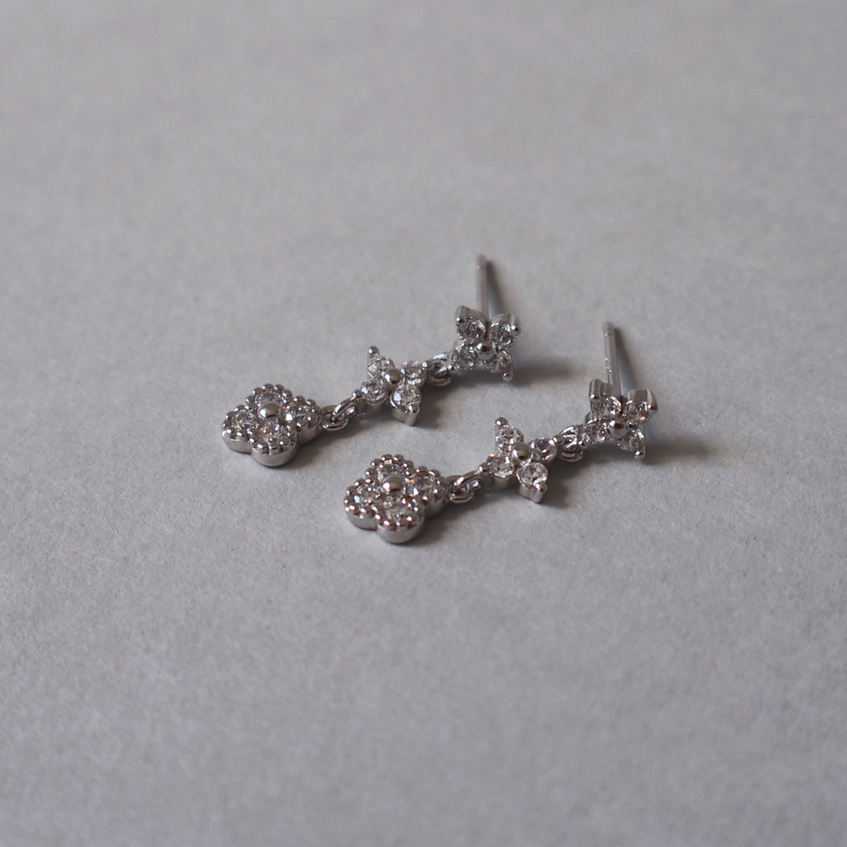 925 sterling silver dangle stud earrings featuring a linked floral motif set with clear cubic zirconia. Detailed photo of the jewelry resting on a light neutral background