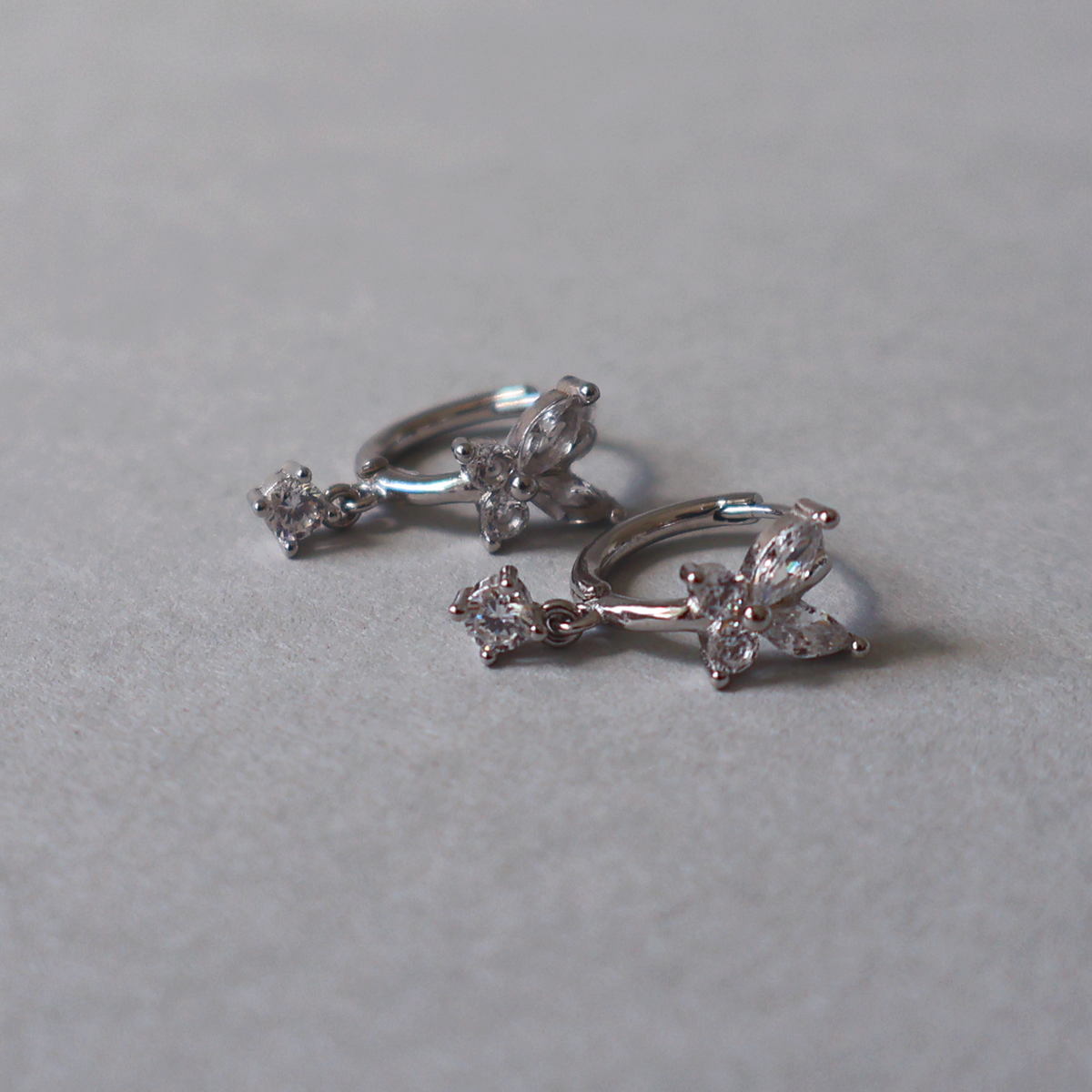 925 sterling silver hoop earrings featuring a butterfly design with clear cubic zirconia and a small dangling stone. Detailed photo of the jewelry resting on a light neutral background