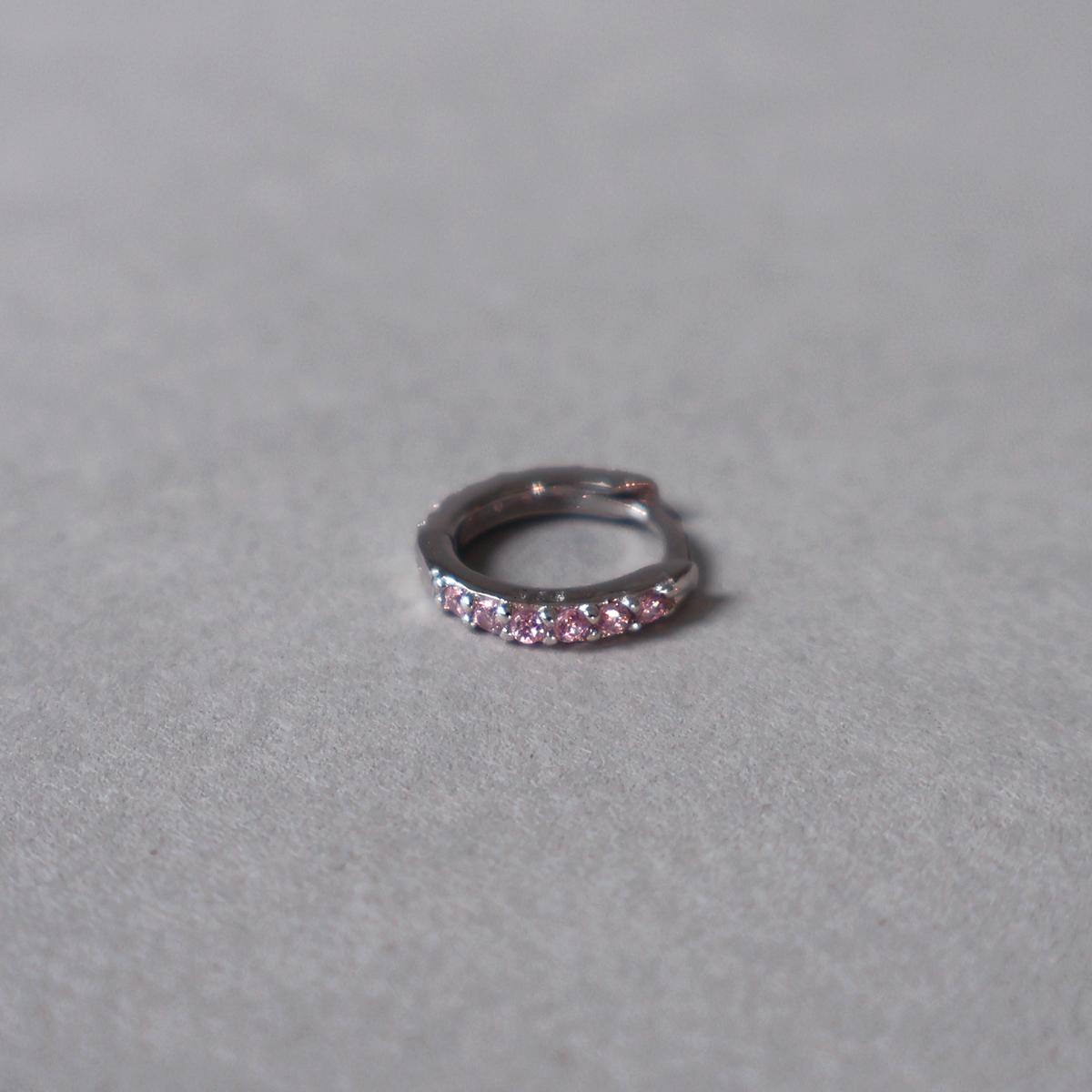 925 sterling silver huggie hoop earring set with a row of light pink cubic zirconia. Detailed photo of the jewelry resting on a light neutral background.