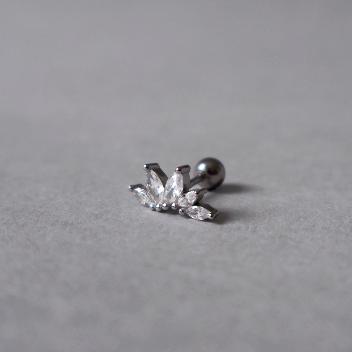 Silver piercing stud with a ball closure, featuring five clear cubic zirconia stones shaped like small leaves arranged in a lotus flower or fan design. Detailed photo of the jewelry resting on a light neutral background.
