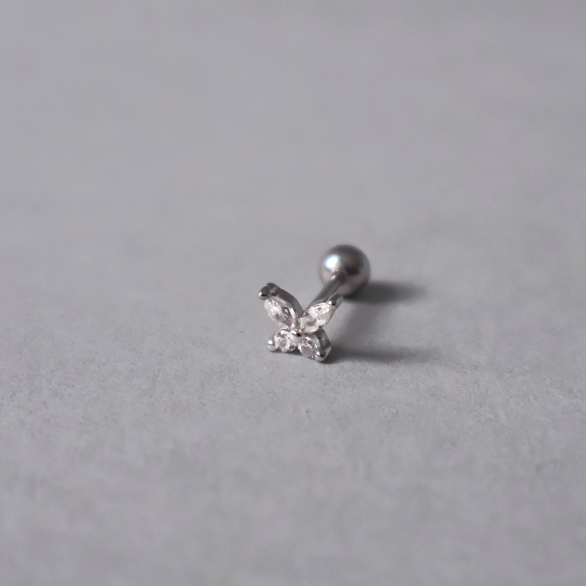 Silver piercing stud featuring a delicate butterfly design set with clear cubic zirconia. Detailed photo of the jewelry resting on a light neutral background.