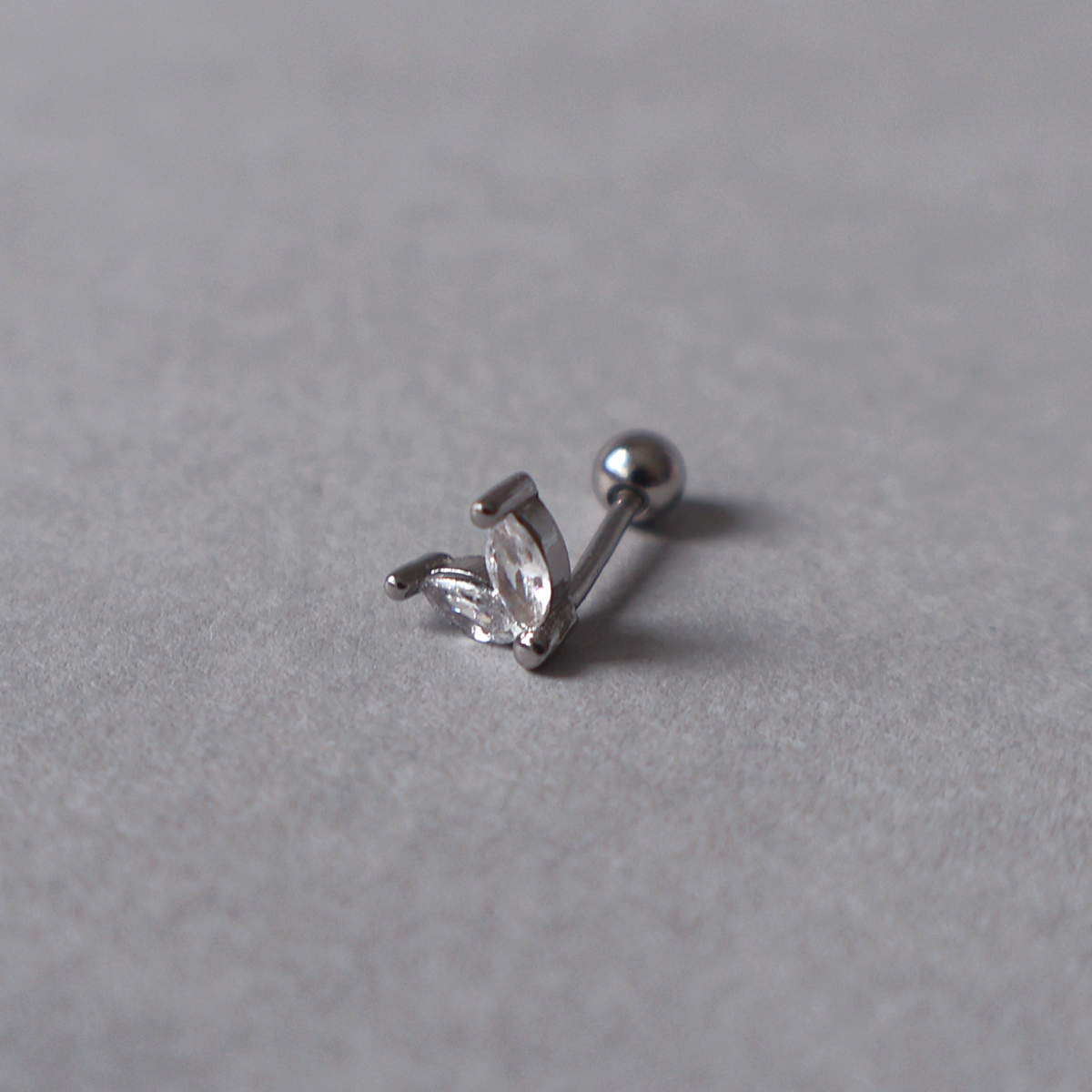 Silver piercing stud featuring a delicate two-leaf design set with clear cubic zirconia. Detailed photo of the jewelry resting on a light neutral background.