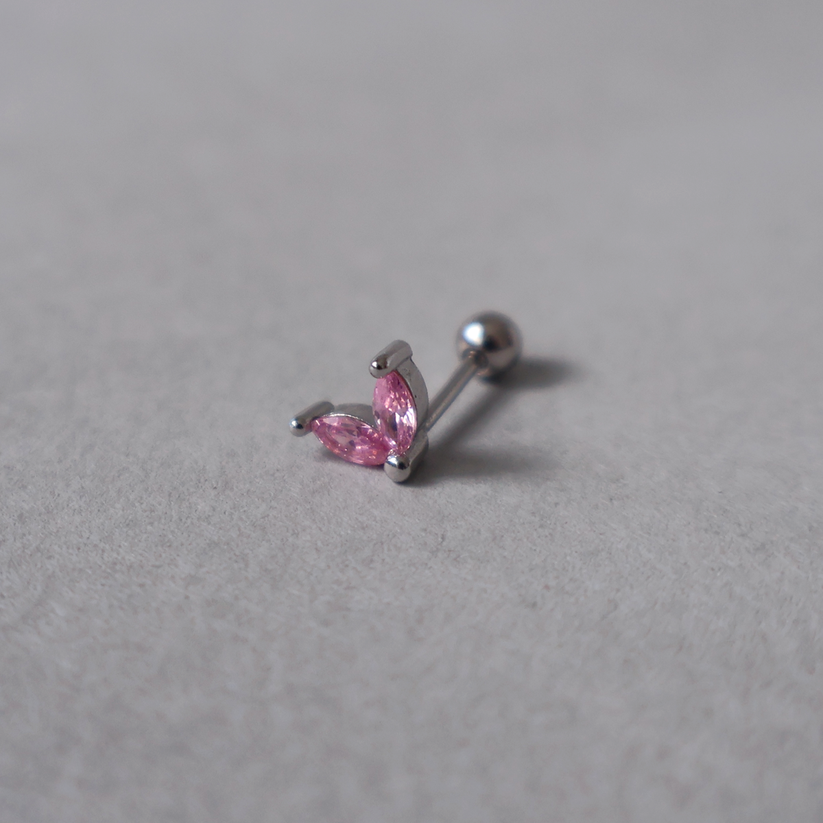 Silver piercing stud featuring a delicate two-leaf design set with pink cubic zirconia. Detailed photo of the jewelry resting on a light neutral background.