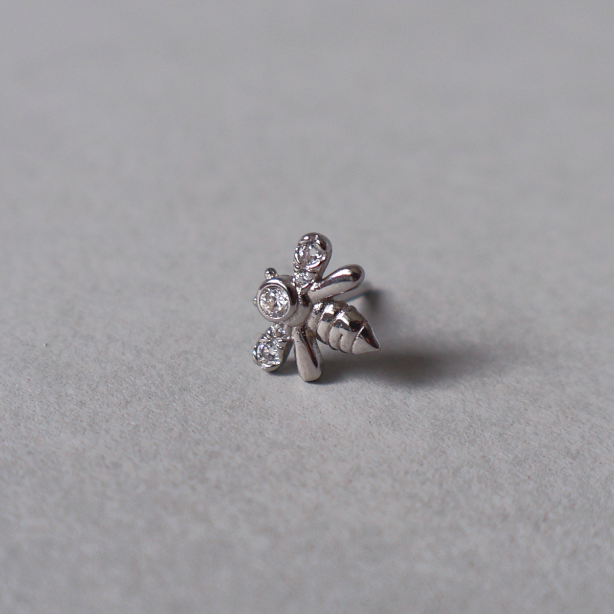 Silver stud earring featuring a small bee design adorned with clear cubic zirconia on its wings and body. Detailed photo of the jewelry resting on a light neutral background.