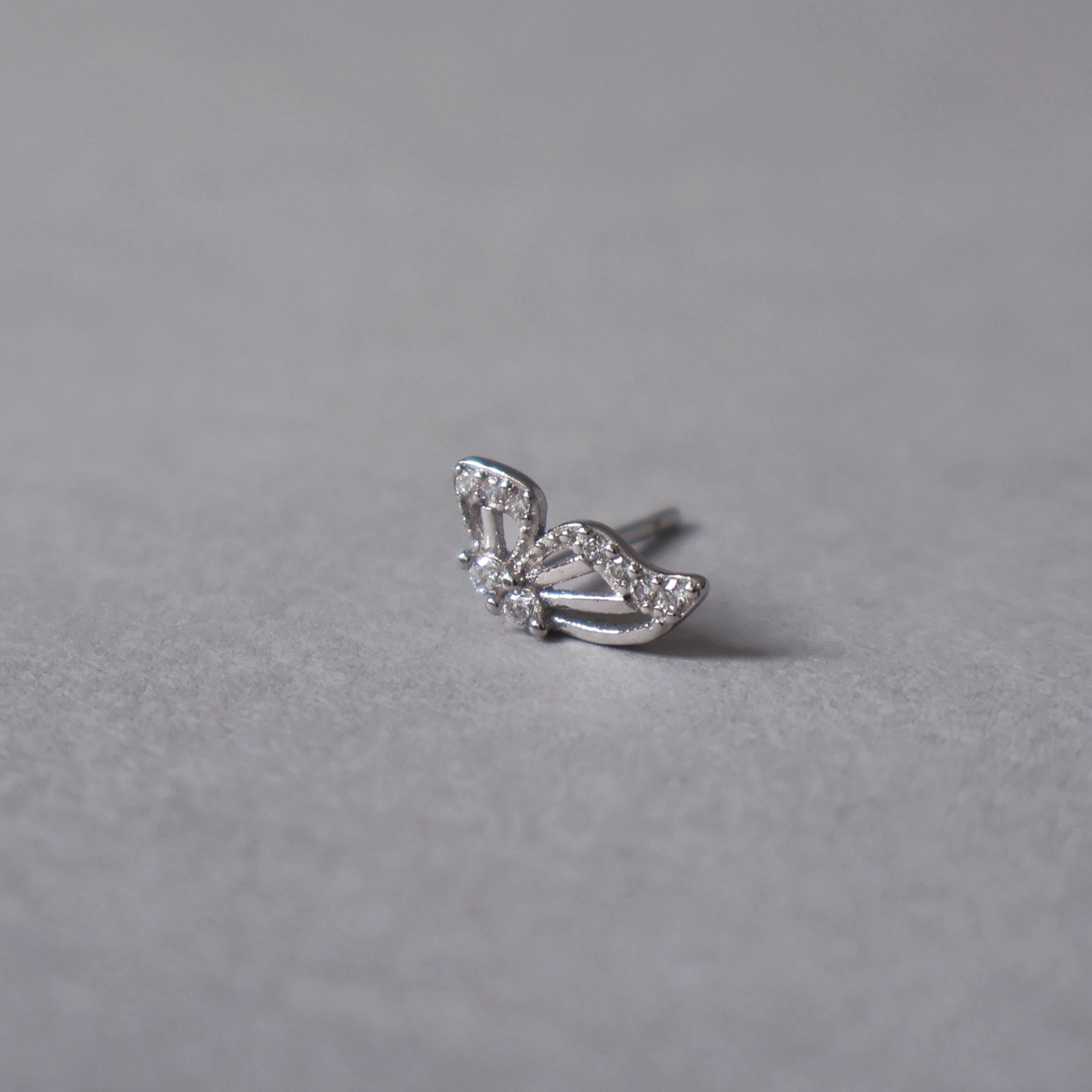 Silver stud earring with a butterfly motif, featuring openwork wings outlined with clear cubic zirconia. Detailed angled photo of the jewelry resting on a light neutral background.