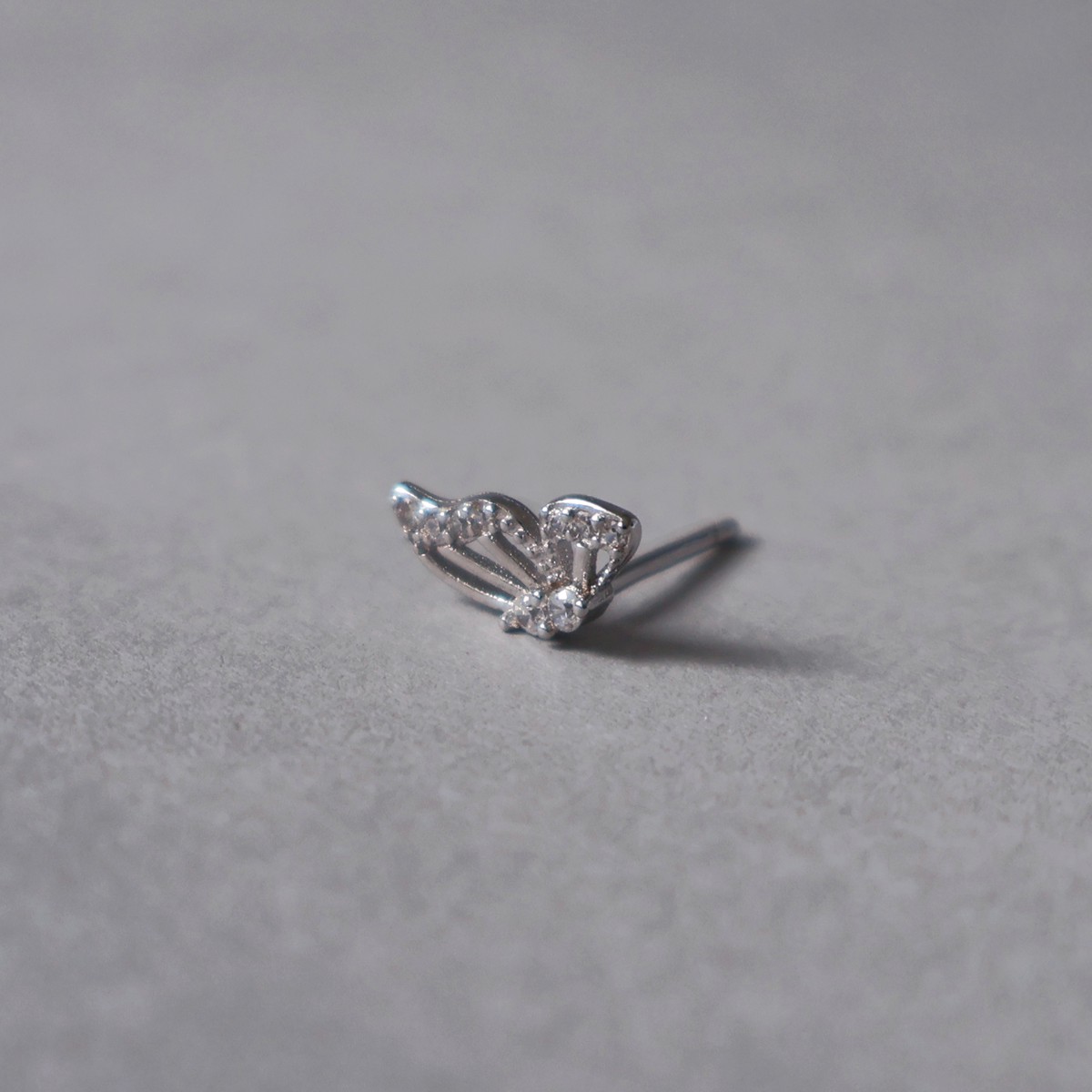 Silver stud earring featuring a delicate butterfly design with cutouts and clear cubic zirconia detailing on the wings and body. Detailed photo of the jewelry resting on a light neutral background.