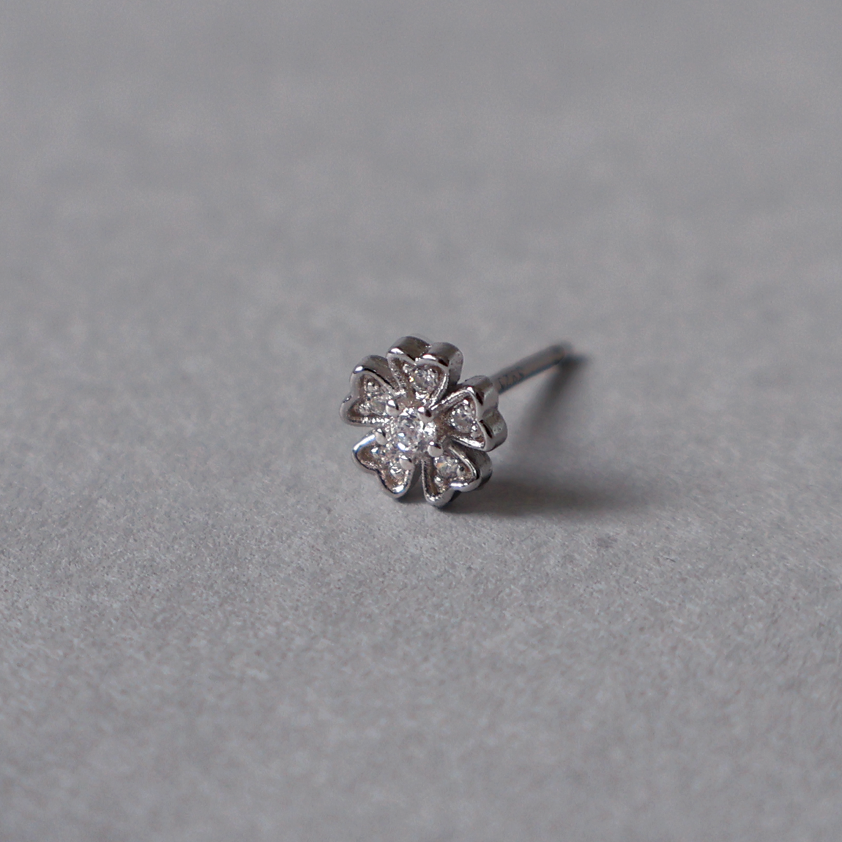 Silver stud earring featuring a delicate five-petal flower design completely set with clear cubic zirconia. Detailed photo of the jewelry resting on a light neutral background.