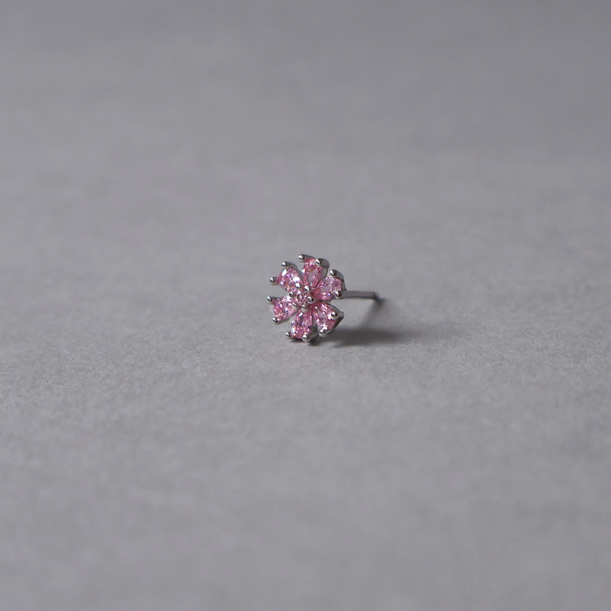 Silver stud earring featuring a flower design set with light pink cubic zirconia. Detailed photo of the jewelry resting on a light neutral background.